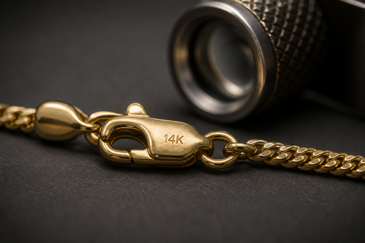 A 14K hallmark stamp on a gold chain clasp with a jeweller's loupe behind it